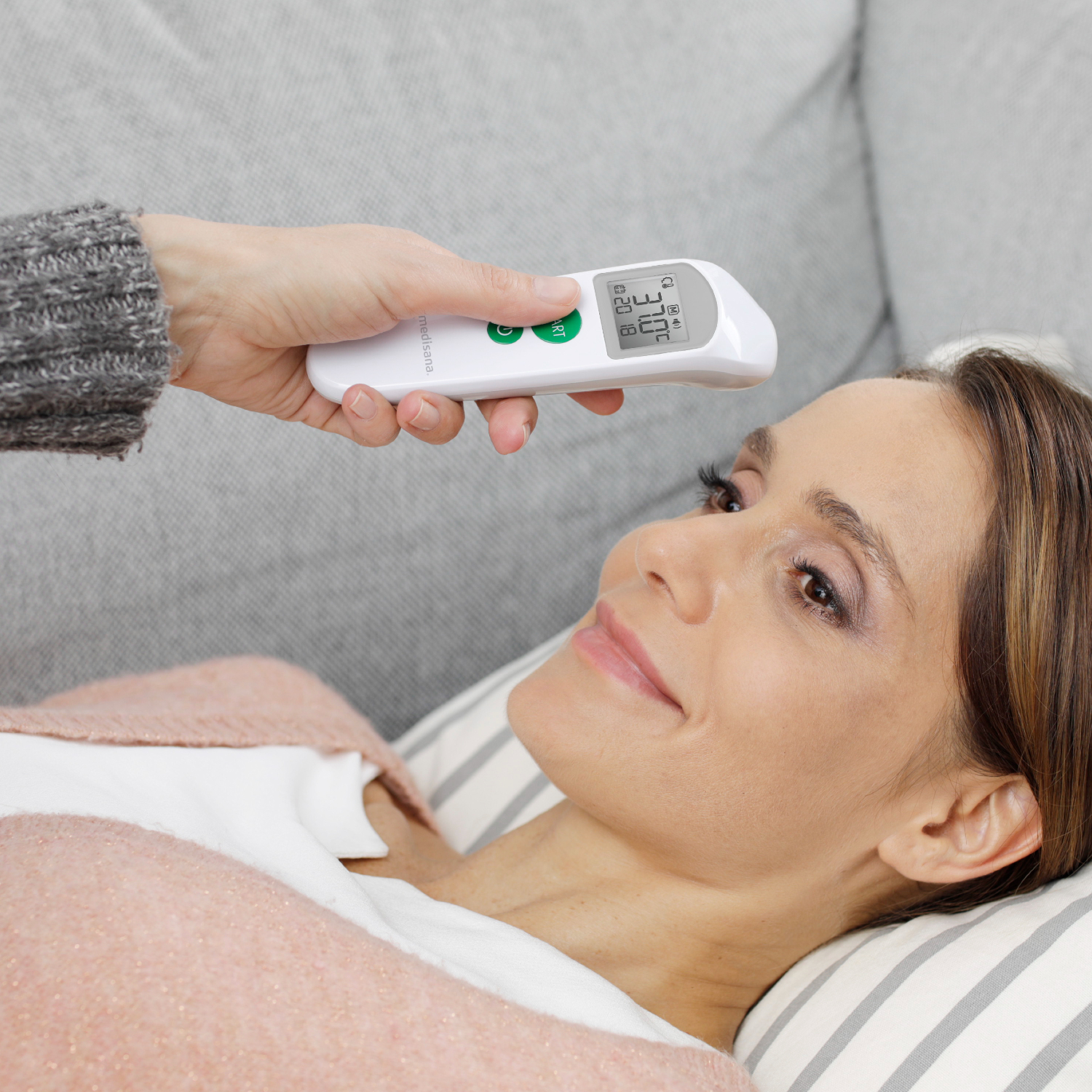 Woman's forehead being checked with a thermometer. White background.