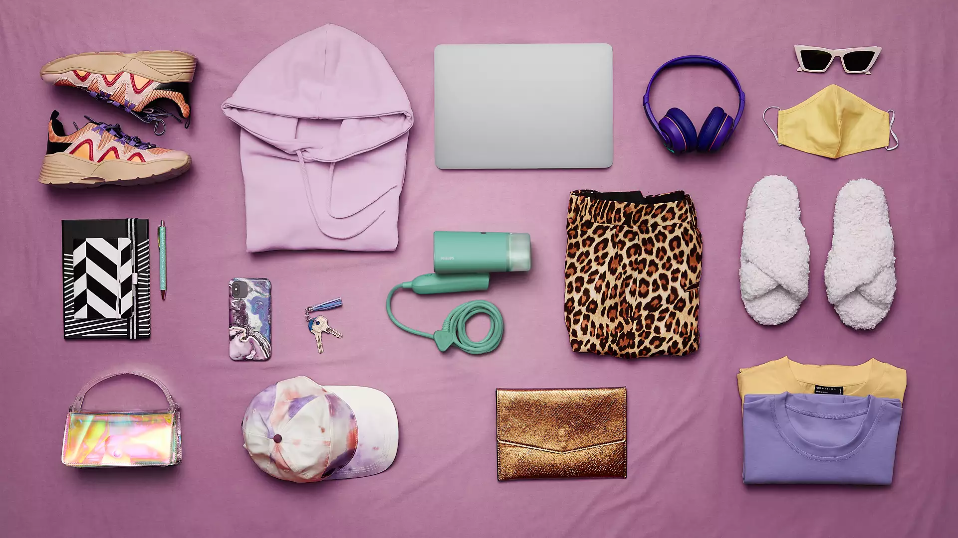 Various items on purple cloth: shoes, hoodie, laptop, headphones, glasses, mask, slippers.
