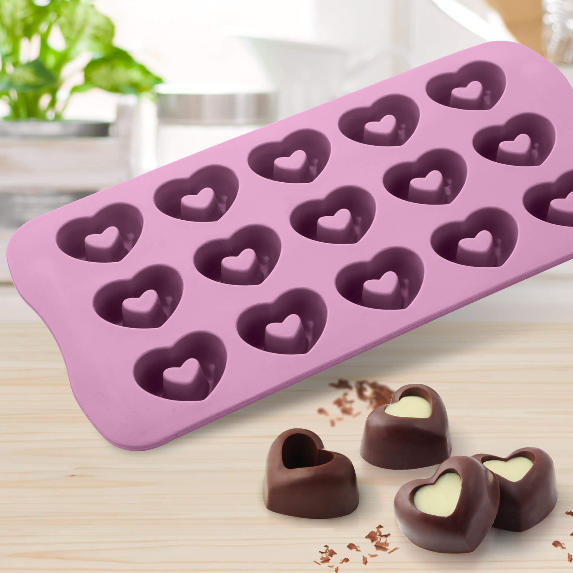 Rosa herzförmige Silikonform. Schokoladenbonbons, drei vorne, auf Holztisch.