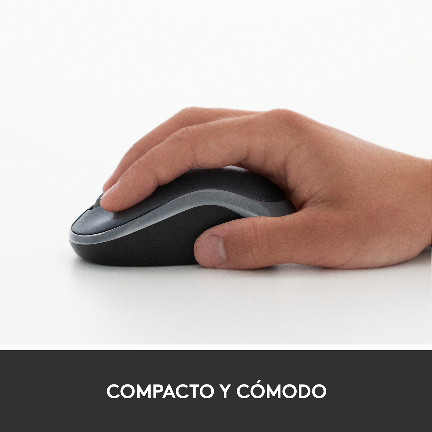 Mano sosteniendo un ratón negro y gris sobre una superficie blanca. El ratón tiene un diseño elegante y ergonómico.