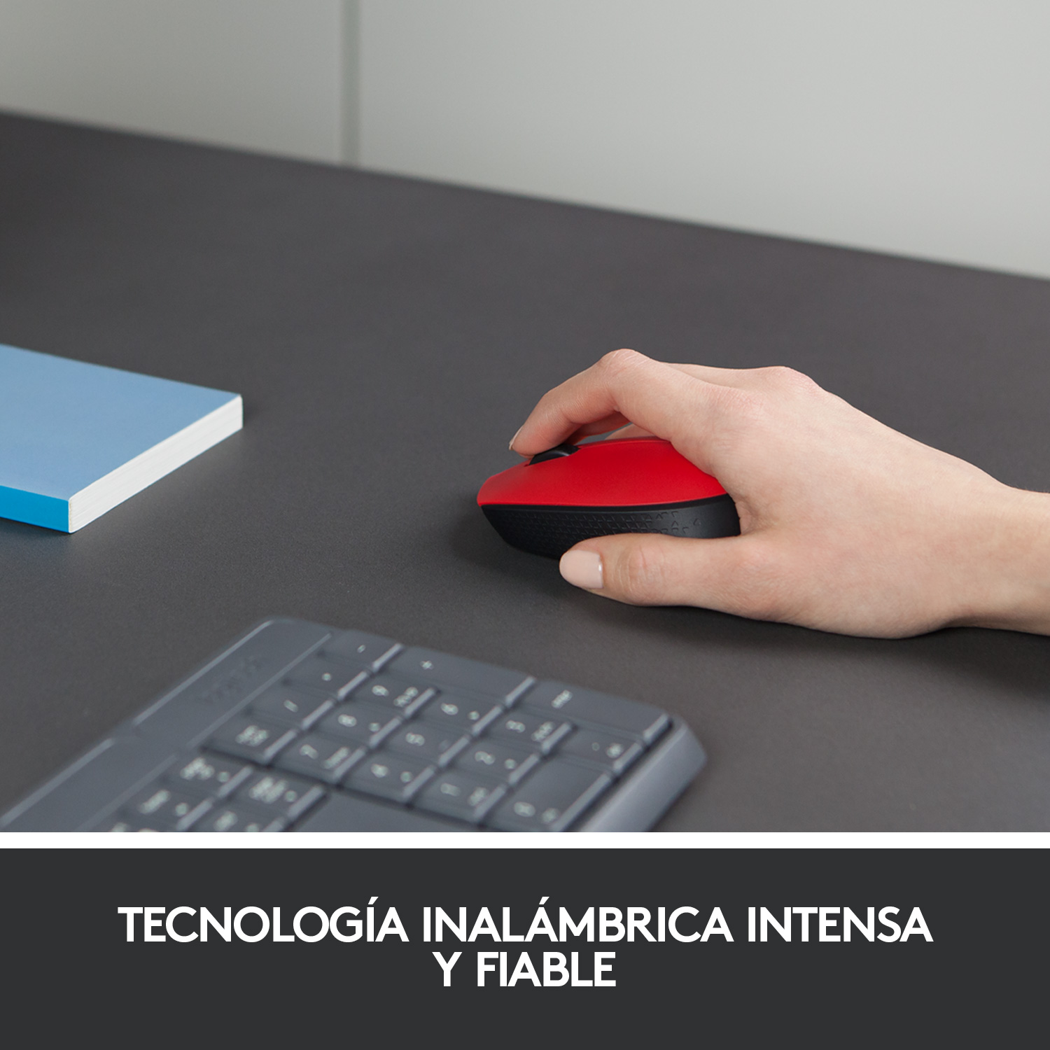 Mano de una persona usando un ratón de ordenador rojo y negro sobre un escritorio oscuro. Teclado abajo.