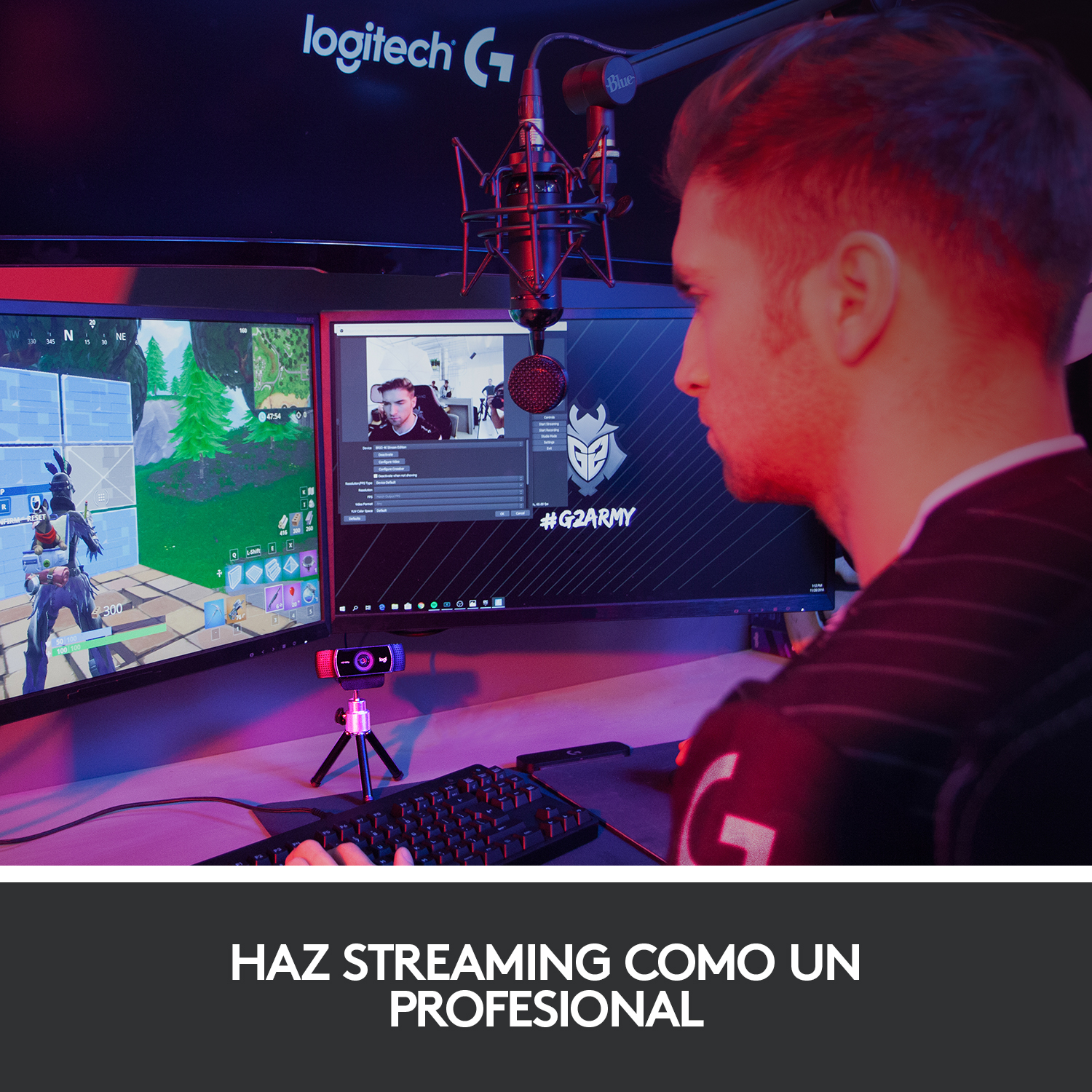 Hombre transmitiendo con dos monitores, micrófono y webcam. Configuración de iluminación roja y azul.