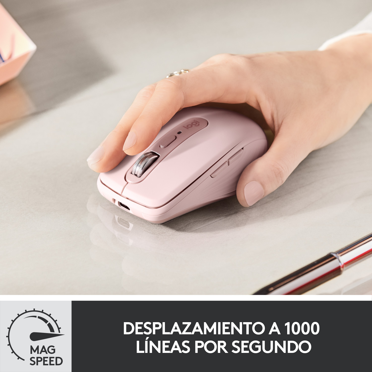 Una persona usando un ratón inalámbrico rosa sobre una superficie gris con un bolígrafo y texto.