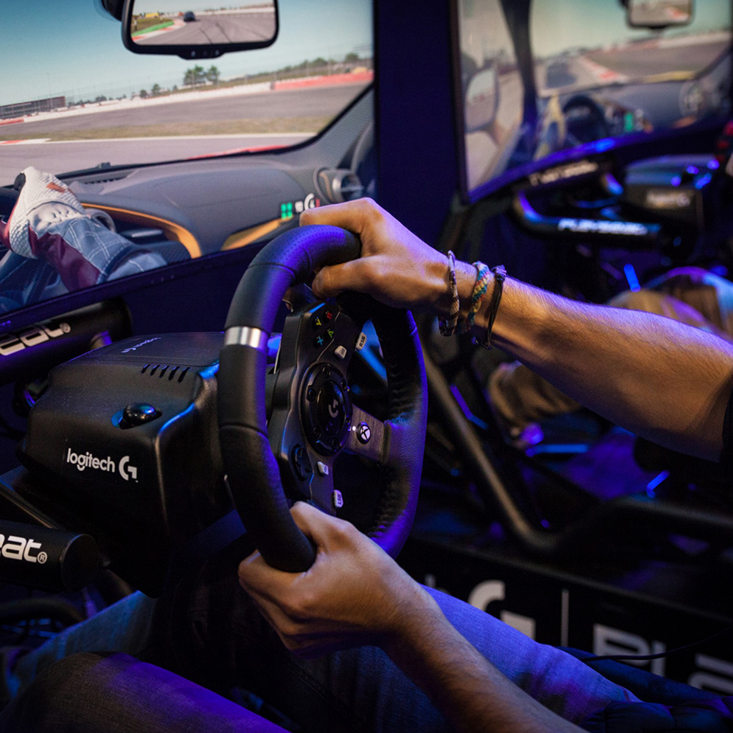 Manos de una persona en un volante de carreras, con pantallas en el fondo.
