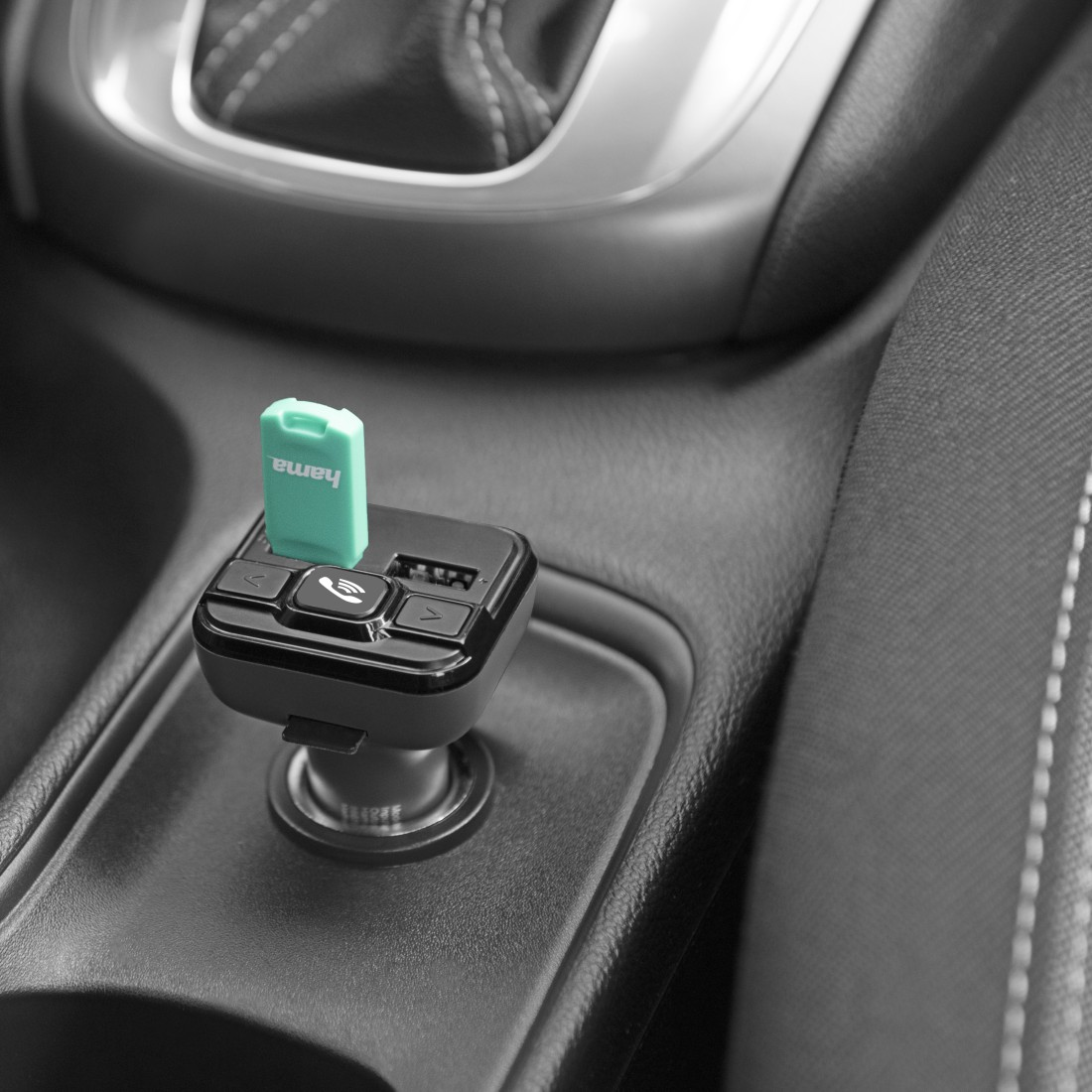 A USB dongle is plugged into a car's power adapter. Black and teal.