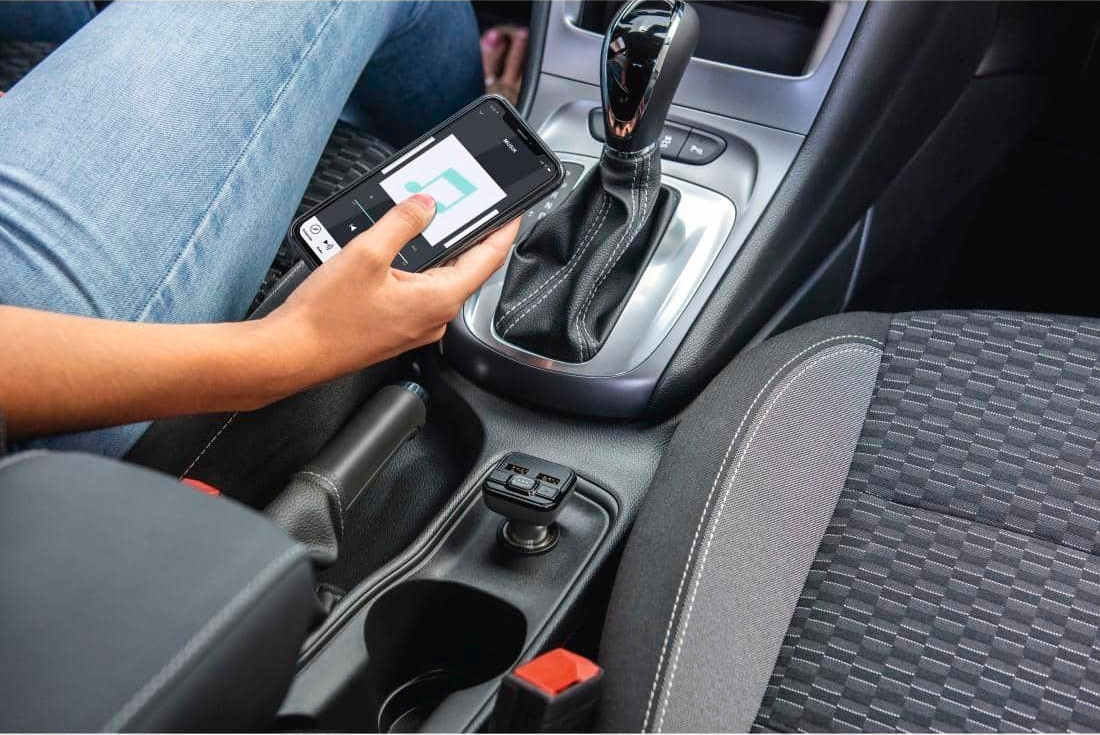 A person in a car holds a phone showing a map app. The gear stick and console are visible.