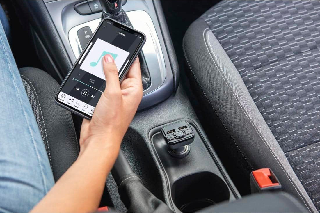 A person's hand holding a phone in a car, next to a car charger.