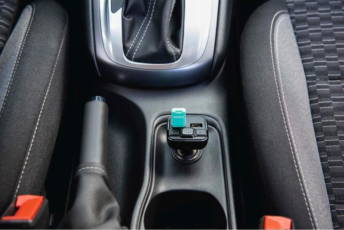 A car's interior with a charger plugged in. A green and black device is in the center console.
