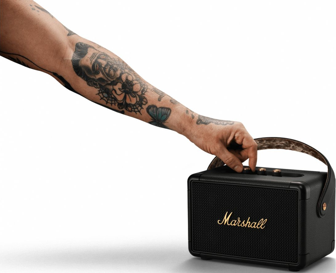Man's arm with tattoos holding a black Marshall speaker, adjusting a knob.