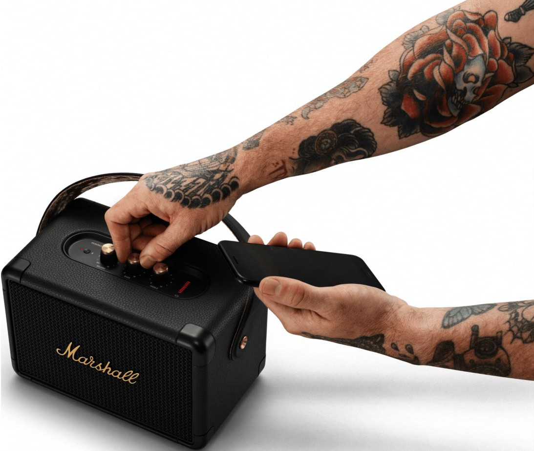A person's hands adjusting the volume of a black Marshall speaker.