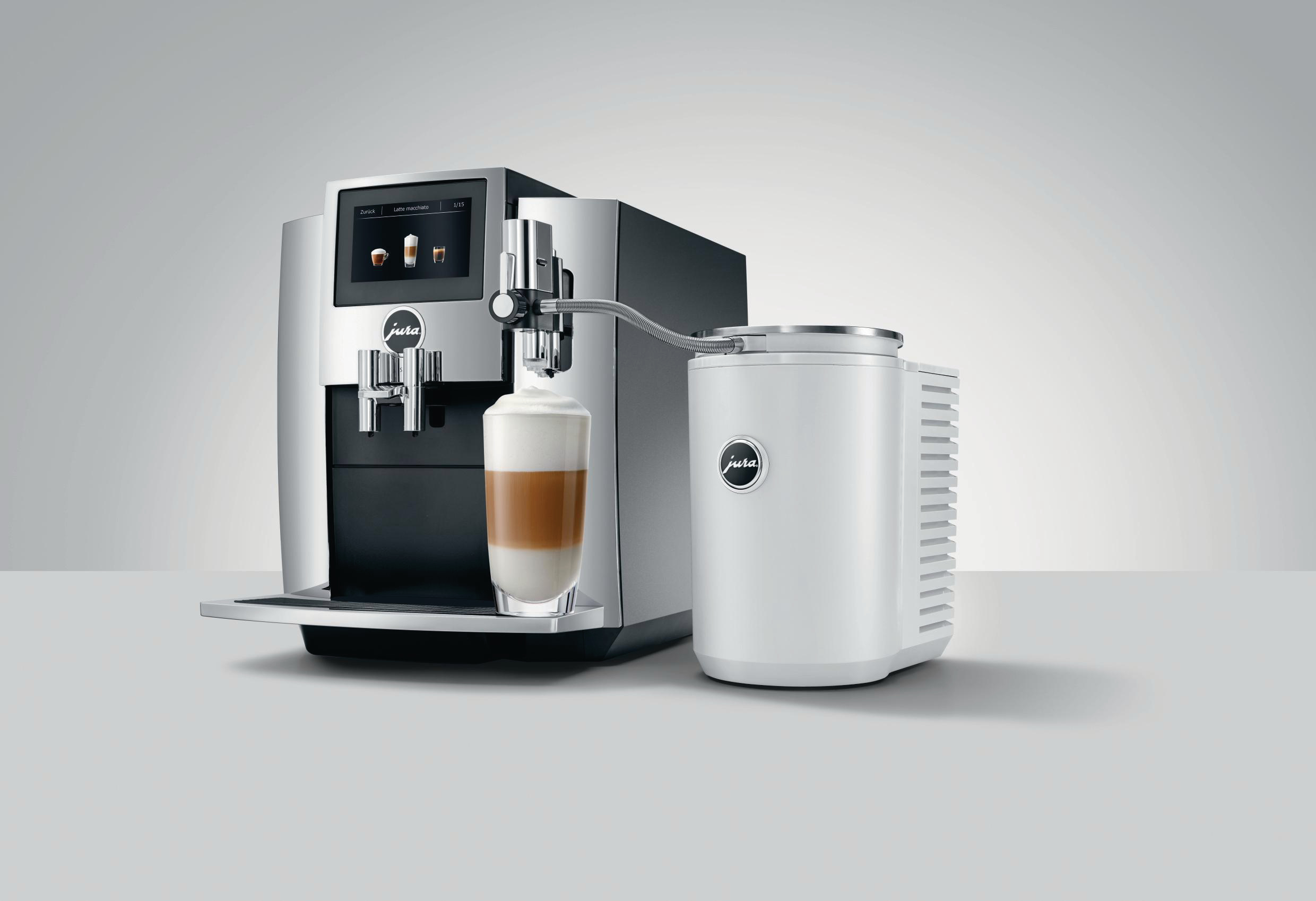 Eine silberne Espressomaschine mit einem Glas Latte Macchiato und einem externen Milchbehälter.