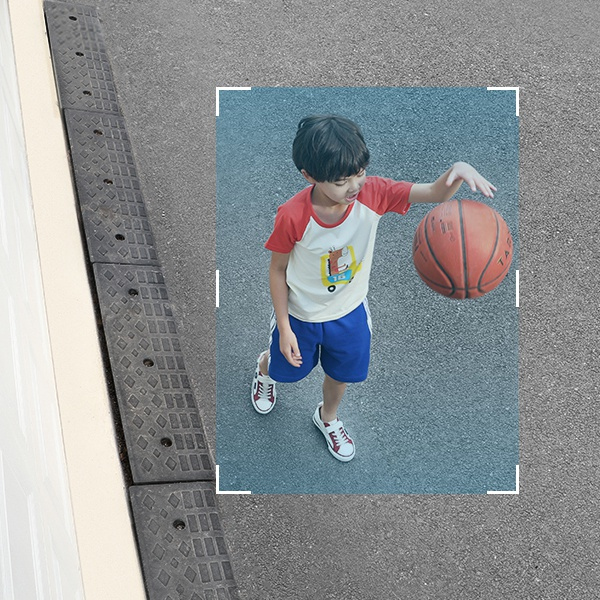 Een jongen in een rood shirt en blauwe korte broek dribbelt met een basketbal op het trottoir.