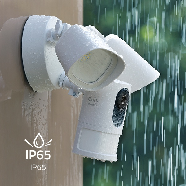 Witte beveiligingscamera en schijnwerpers op een muur gemonteerd, met waterdruppels. Het IP65-teken is zichtbaar.