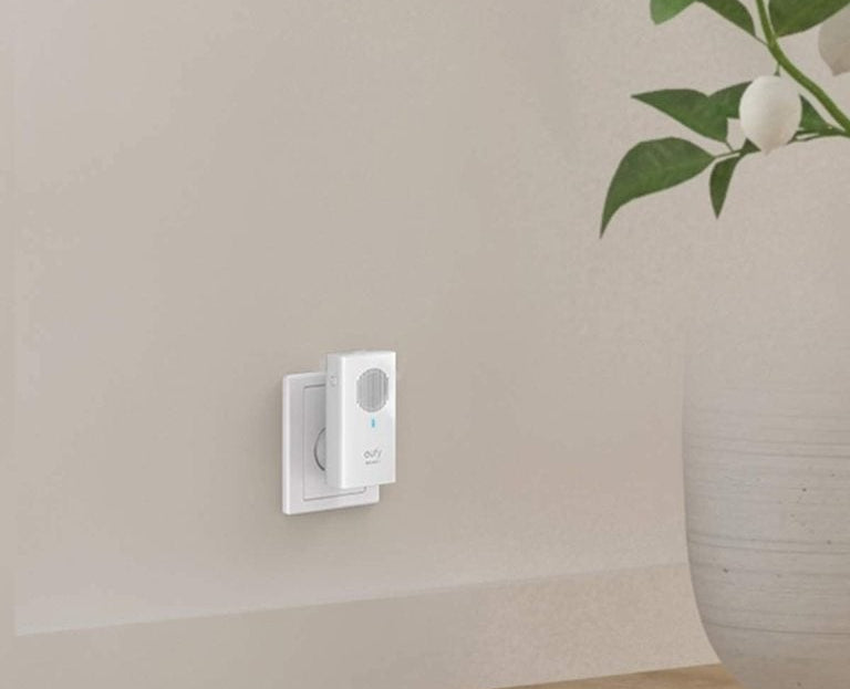 Une sonnette intelligente blanche branchée sur une prise murale sur un mur beige clair.