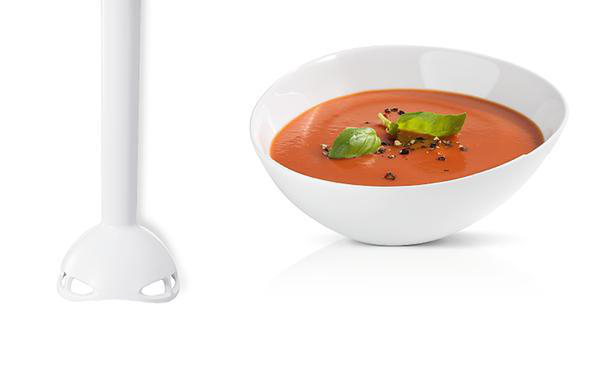Ein weißer Stabmixer neben einer weißen Schüssel mit Tomatensuppe, garniert mit Basilikum.
