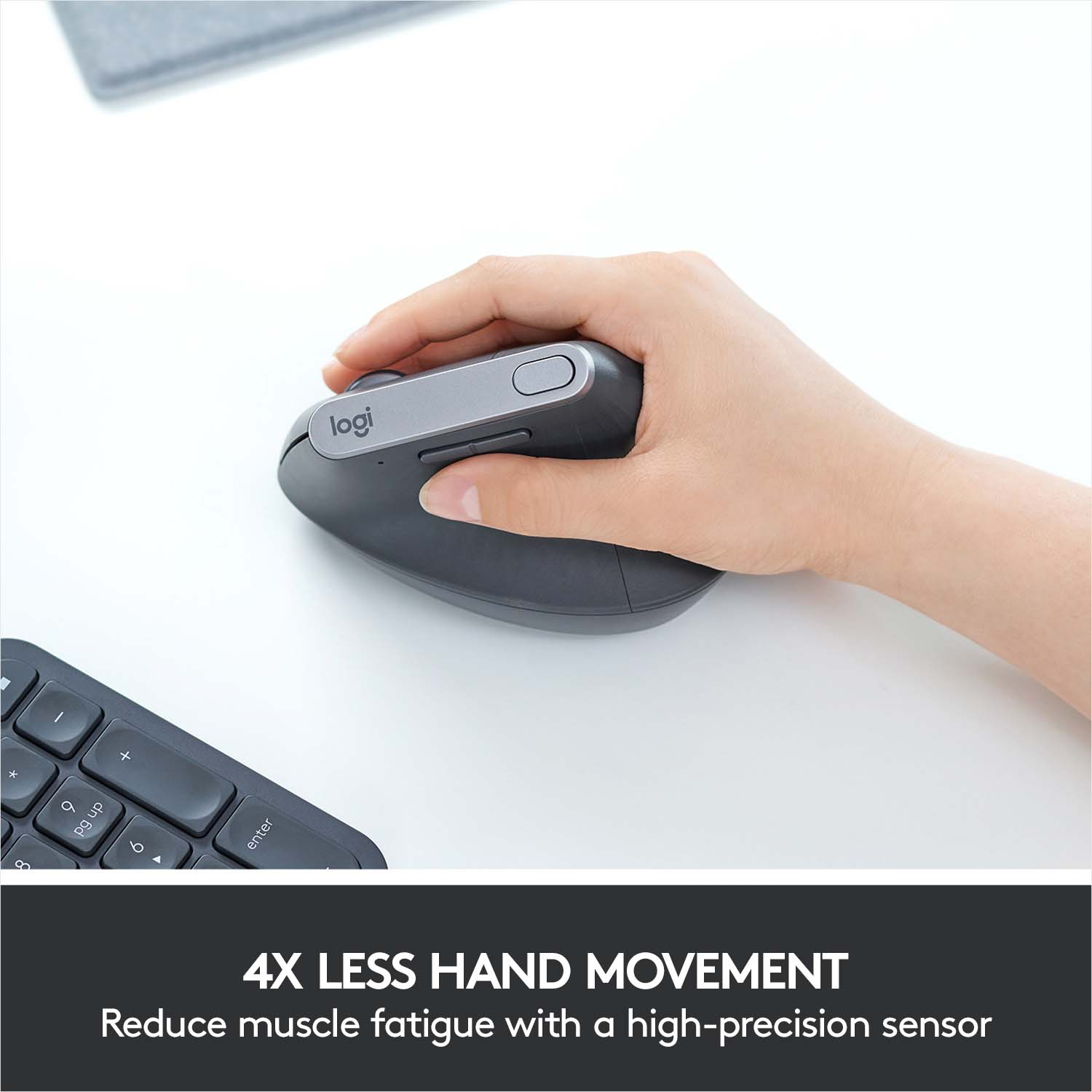 Une main utilise une souris ergonomique grise sur une surface blanche à côté d'un clavier.