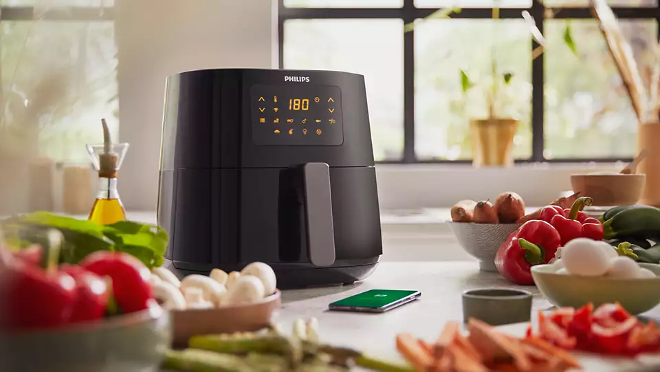 Une friteuse à air noire avec un écran numérique et des légumes sur un comptoir de cuisine.