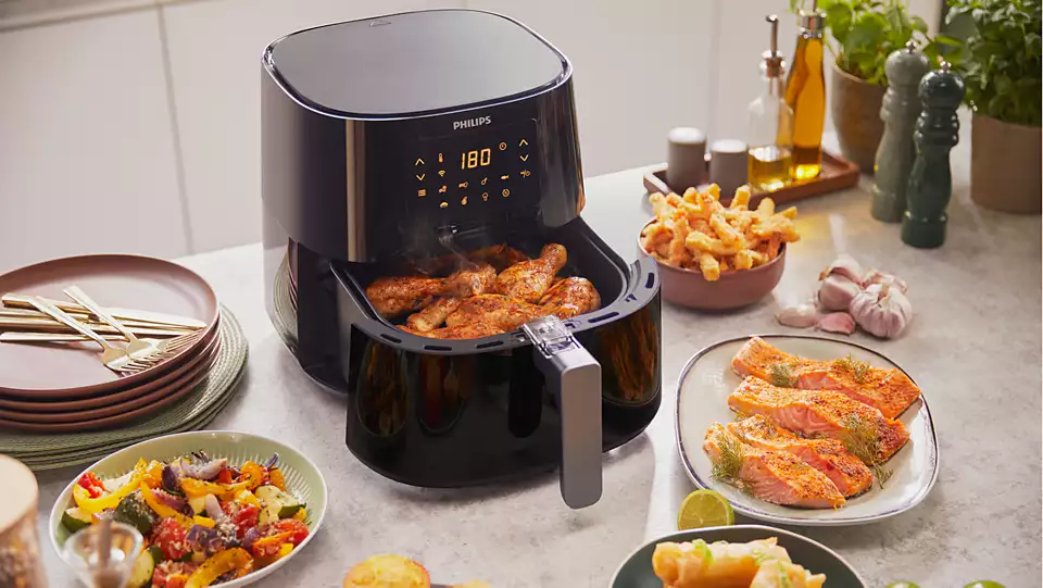 Friteuse à air avec poulet et saumon cuits, ainsi que des légumes.