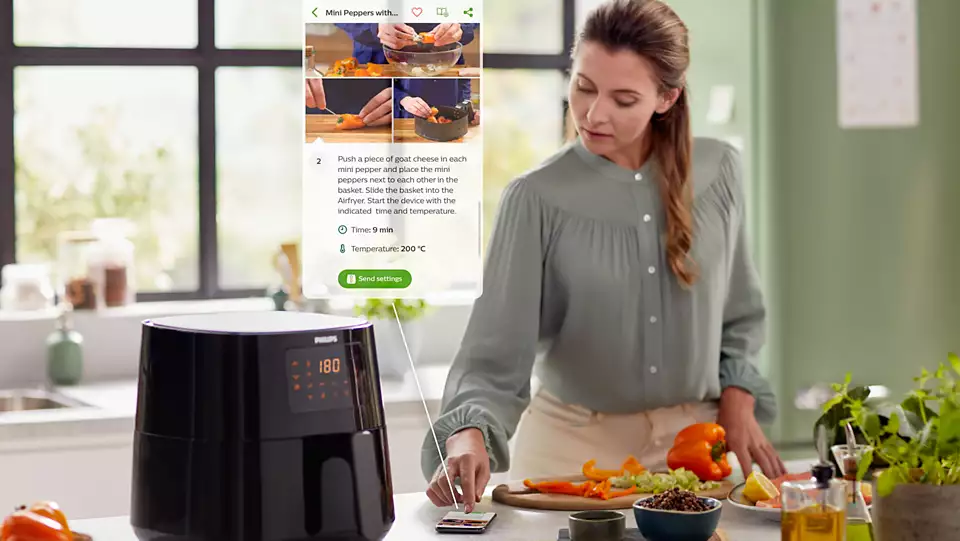 Femme près d'une friteuse à air, regardant un téléphone avec une recette.