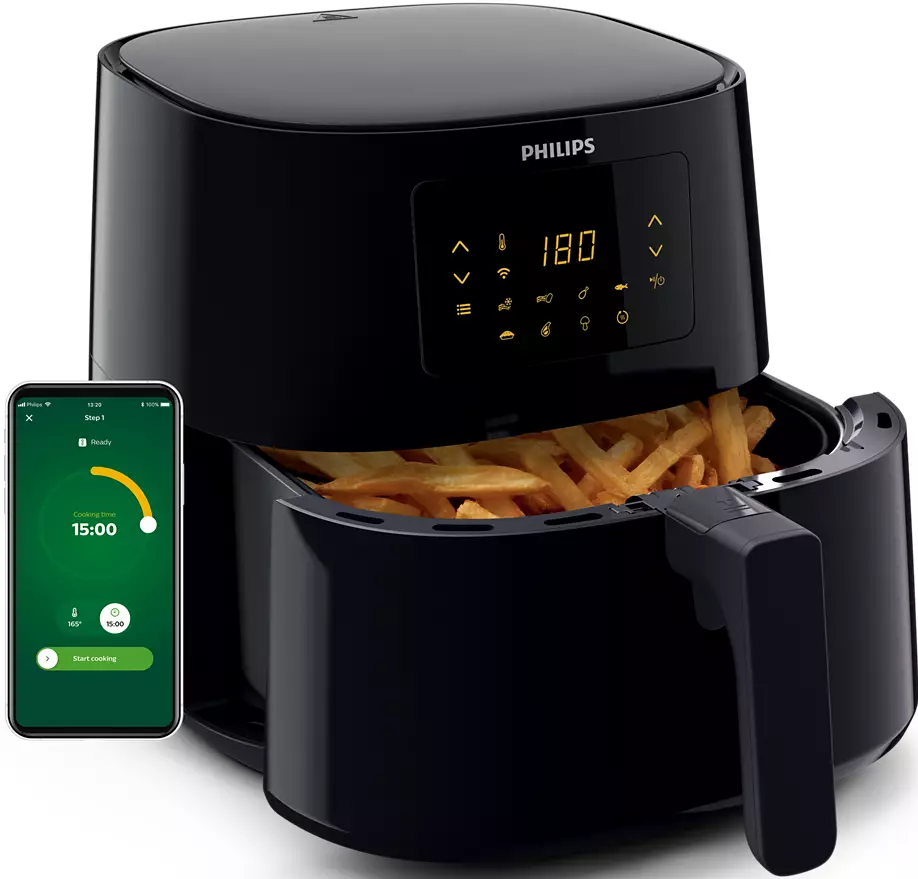 Une friteuse à air noire avec un téléphone affichant une application. Des frites sont dans la friteuse.