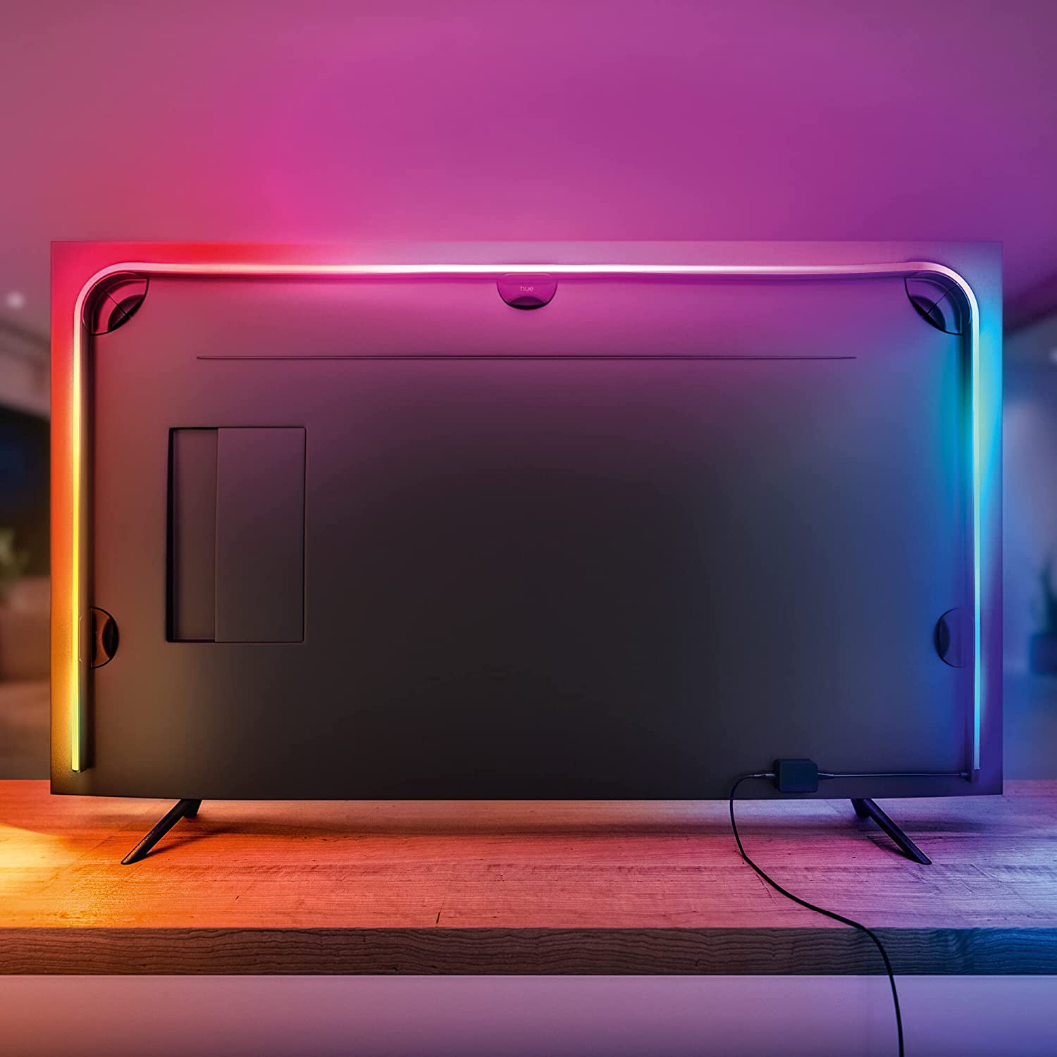 Kenarlarında renkli LED ışıkları olan büyük bir TV'nin arkası. TV ahşap bir yüzey üzerinde.