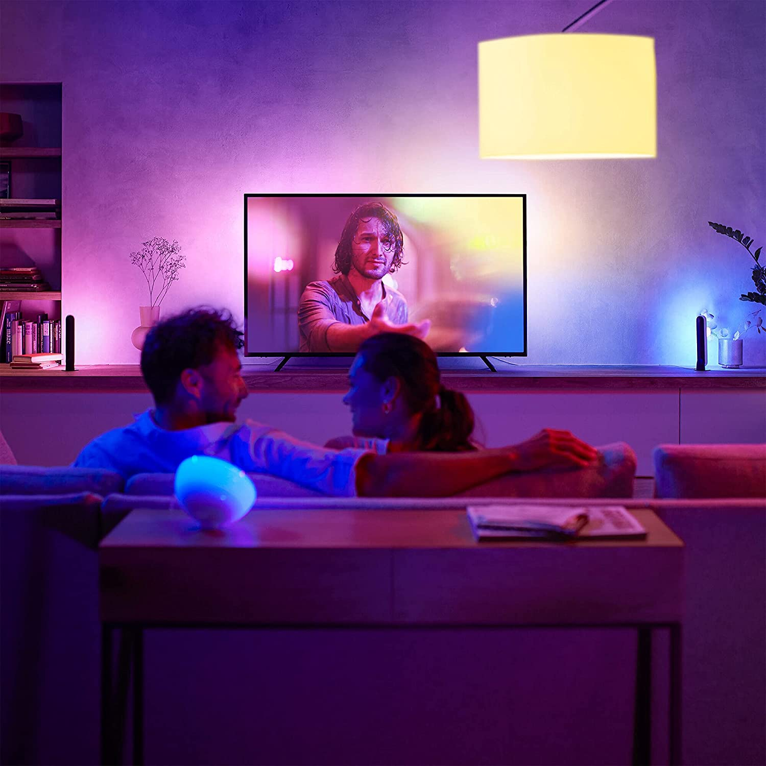 Bir çift kanepeye oturmuş televizyon izliyor. RGB ışıkları odayı aydınlatıyor.