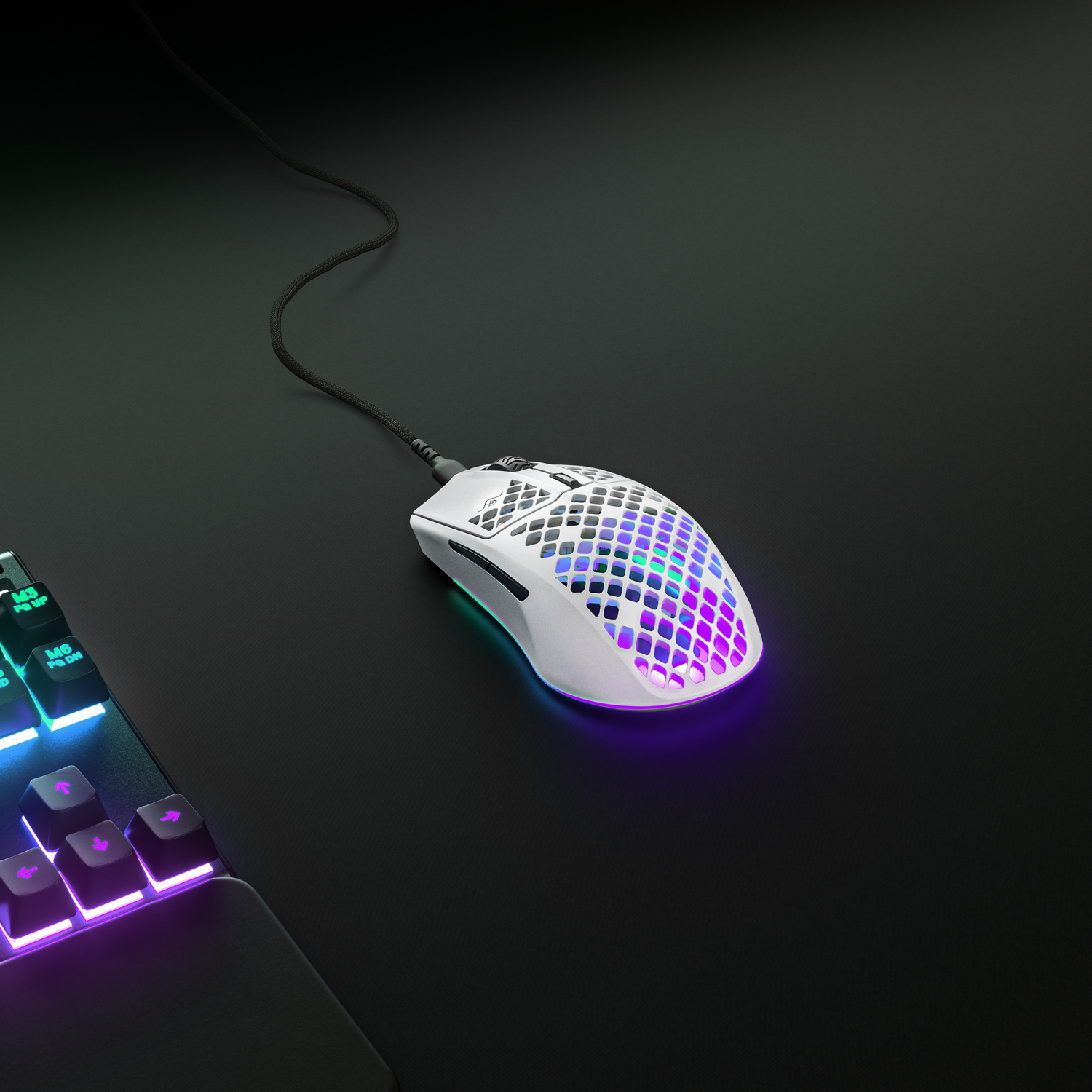 Ratón gaming blanco con luces de colores. Cable conectado, sobre superficie negra con teclado.