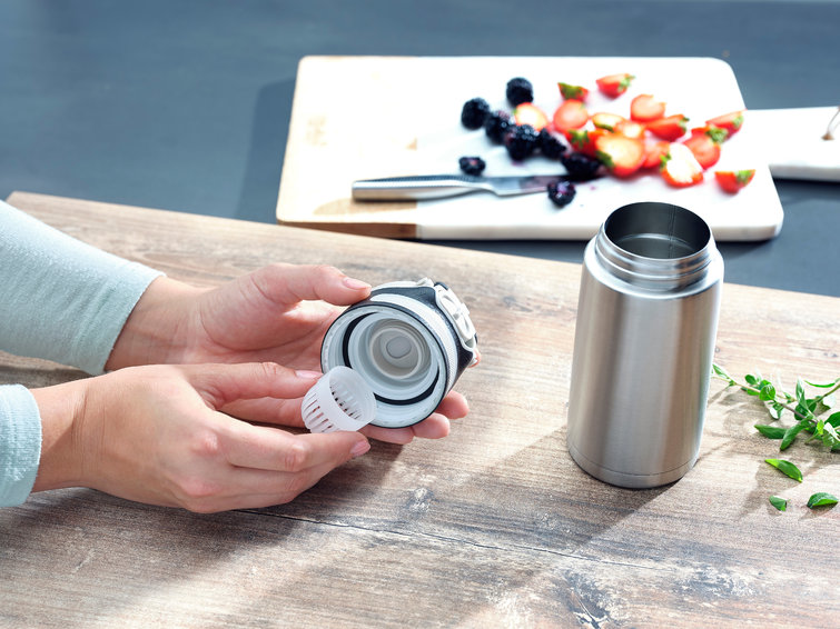A person's hands are holding the parts of a container. The container is stainless steel.