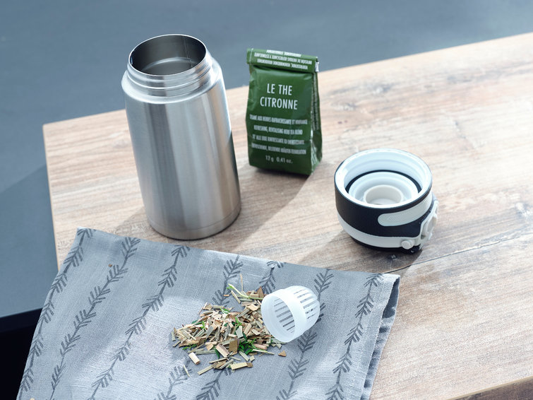 Stainless steel water bottle, open, with tea and a green tea bag.