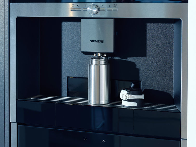 A built-in coffee machine with a steel thermos and a black and white travel mug.