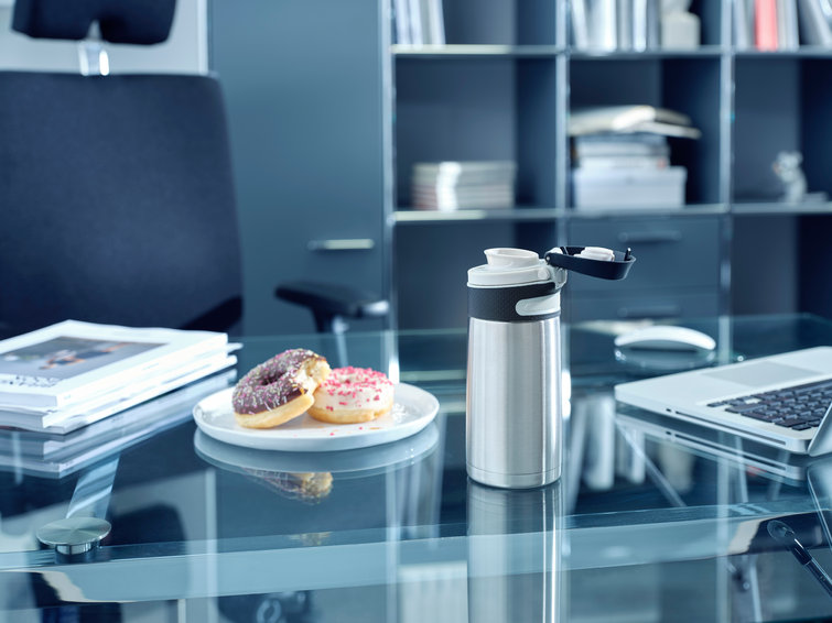 Office desk with a water bottle and two donuts on a plate next to a laptop.