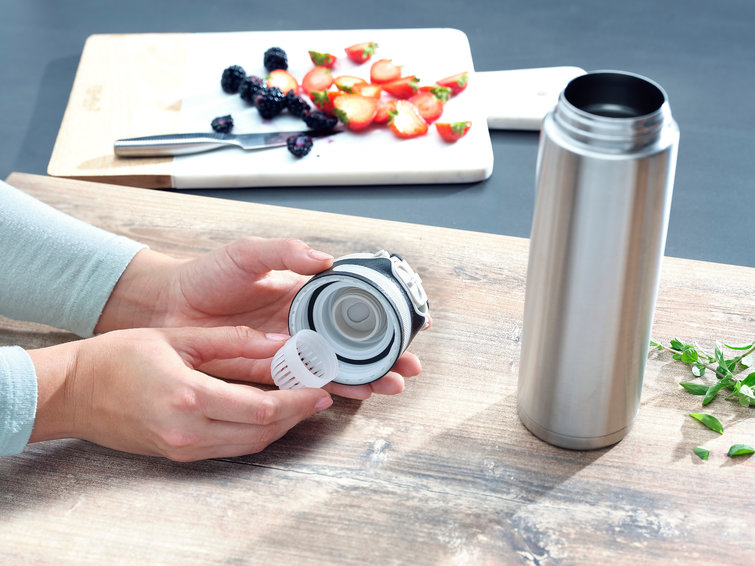 A person's hands disassemble a stainless steel water bottle with sliced strawberries and blackberries.
