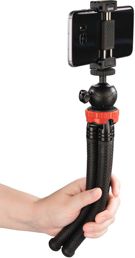 Hand holding a black smartphone in a phone holder. The phone is mounted on a black and red tripod.