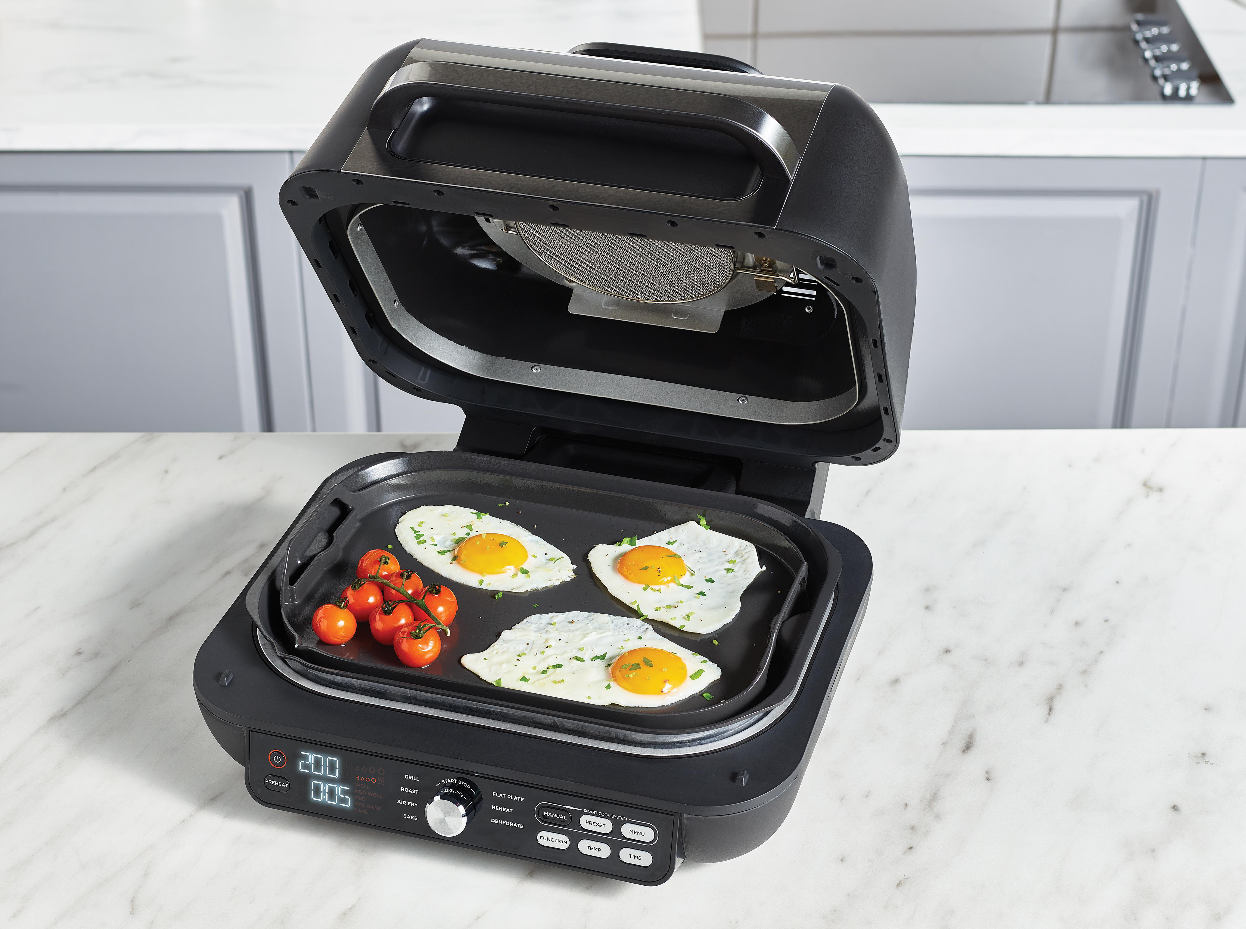 Ein geöffneter schwarzer Grill mit drei Spiegeleiern und Kirschtomaten.