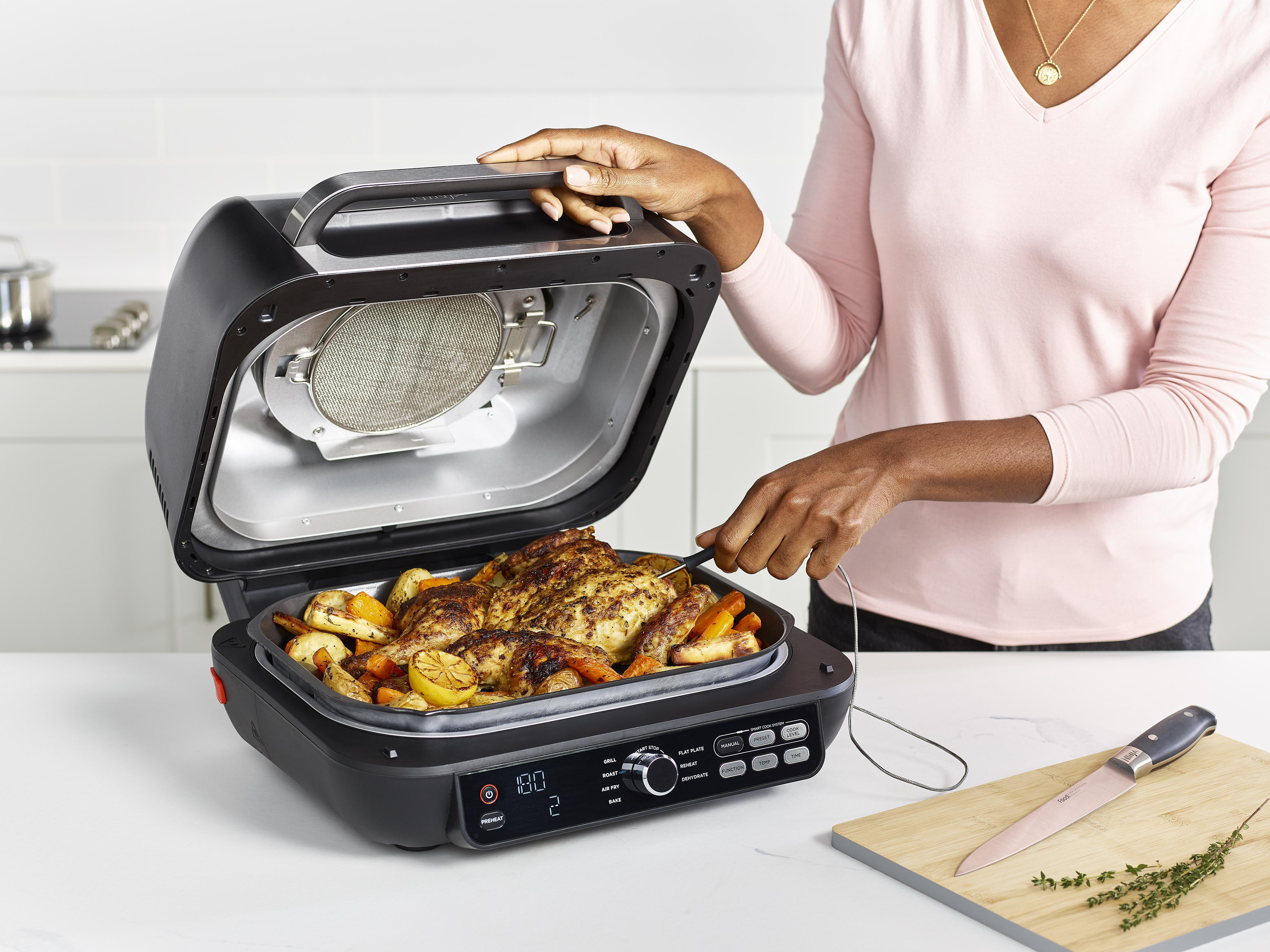 Eine Person prüft ein gebratenes Hähnchen mit Gemüse in einem schwarzen Grill.