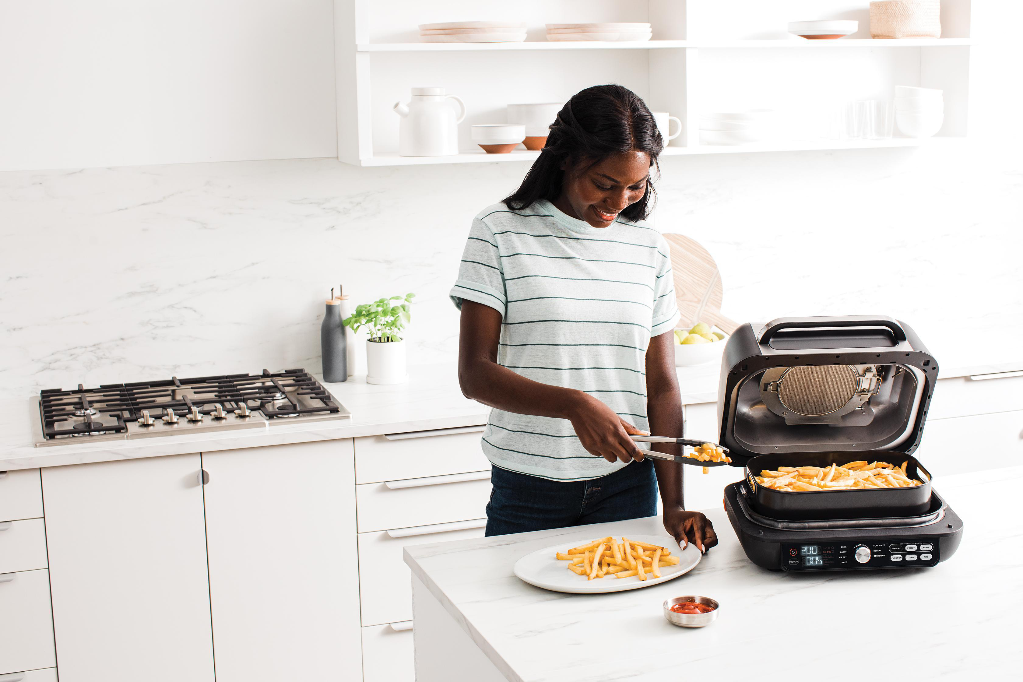 Eine Frau legt Pommes aus einem Airfryer auf einen Teller.