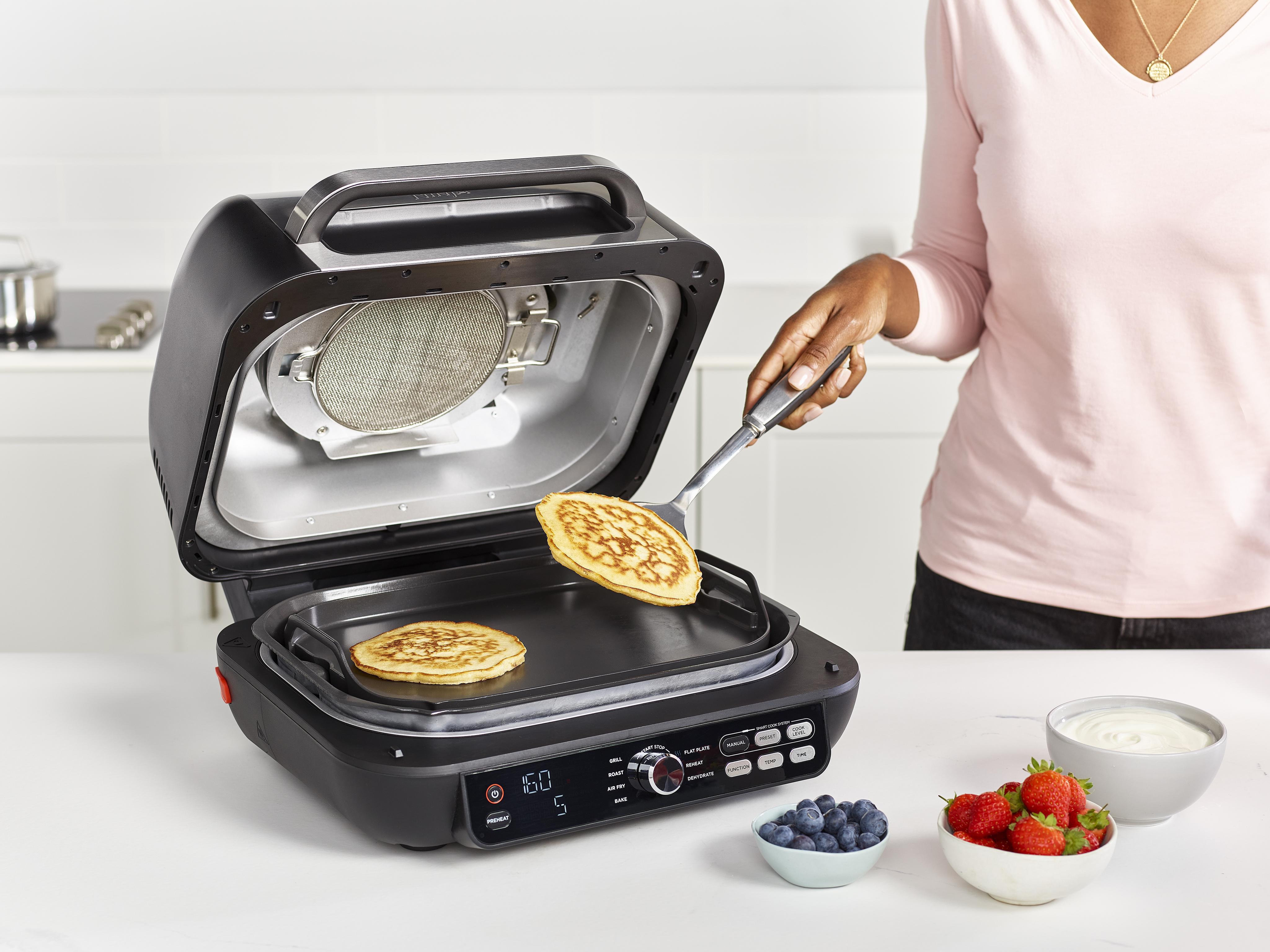 Eine Person benutzt einen Toaster, um Pfannkuchen zuzubereiten. Beeren und Joghurt sind daneben.