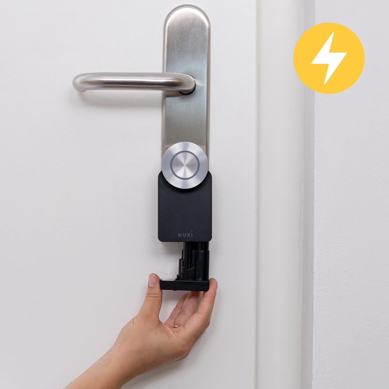 Una mano instalando una cerradura inteligente en una puerta blanca. Un icono de rayo amarillo es visible.