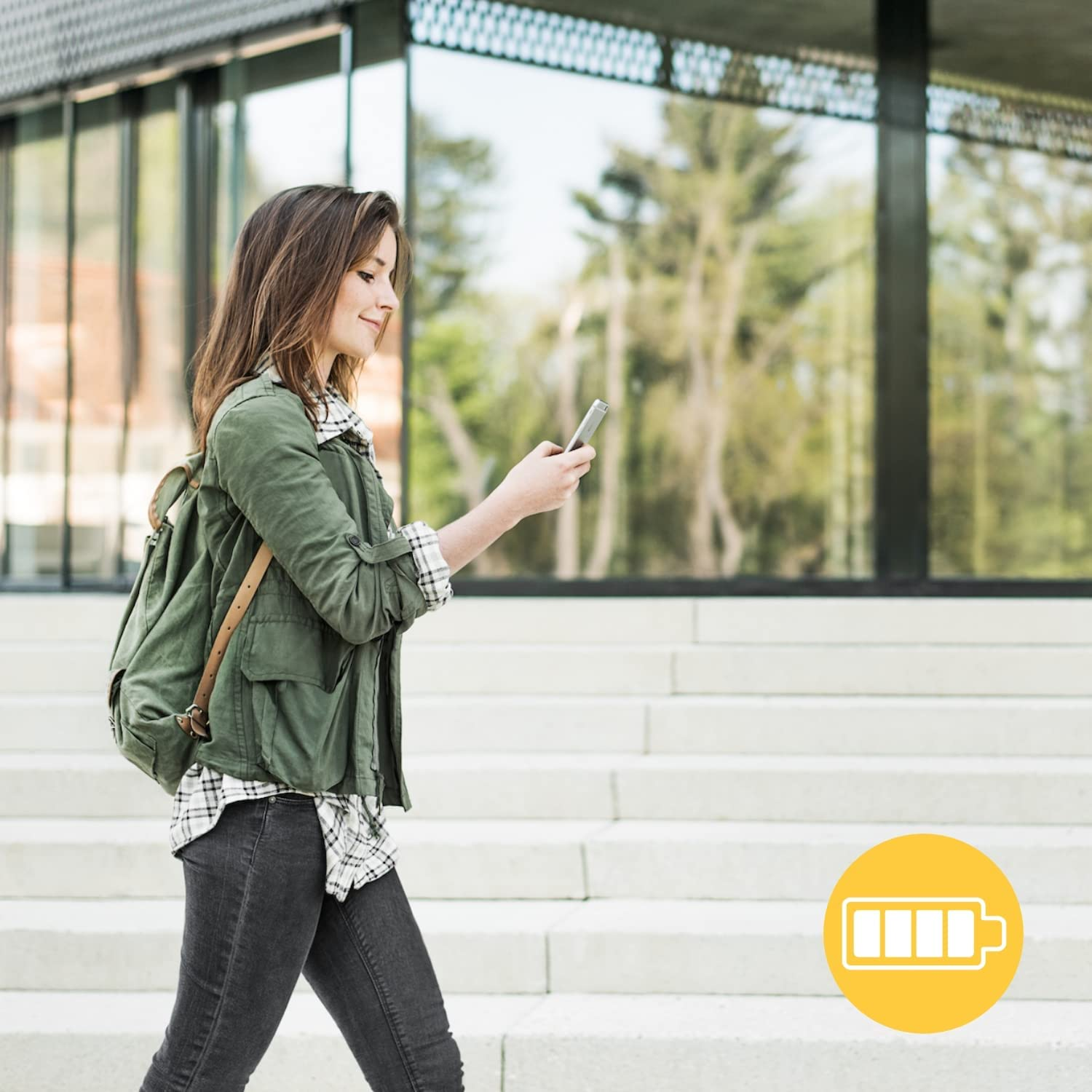 Mujer caminando con teléfono, chaqueta verde, cerca de escaleras, icono de batería.