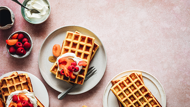 Gofres en platos, cubiertos con fruta y crema. Fondo rosa, vista cenital.