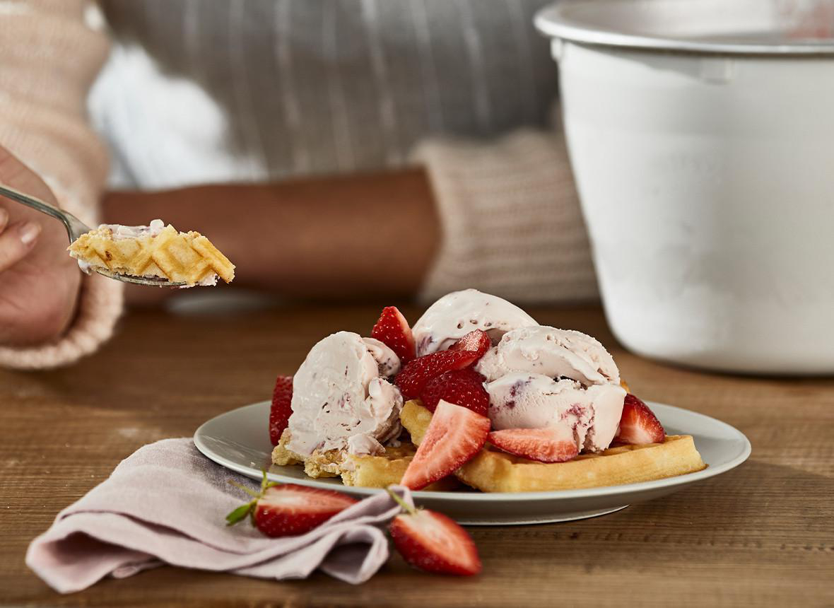 Eine Frau hält einen Teller mit Eis, Erdbeeren und Waffeln.