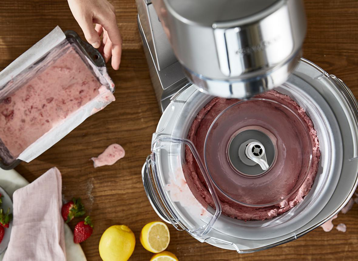 Draufsicht auf eine Maschine, die rosa Eiscreme herstellt, mit Zutaten und einer Hand in der Nähe.