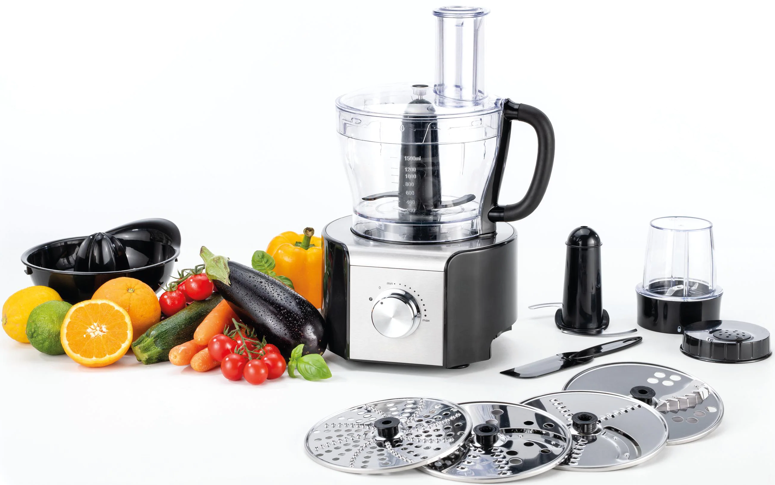Eine Küchenmaschine mit Gemüse und Obst. Enthält eine Saftpresse und mehrere Schneidescheiben.