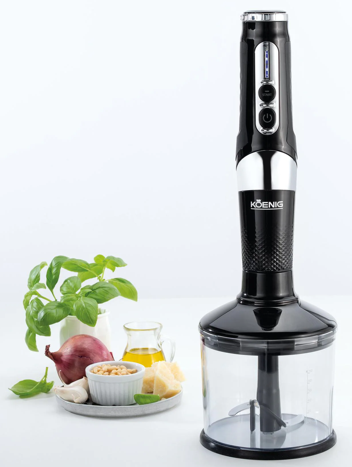 Frullatore a immersione nero e argento con ingredienti: basilico, cipolla, pinoli, olio e parmigiano su una superficie bianca.