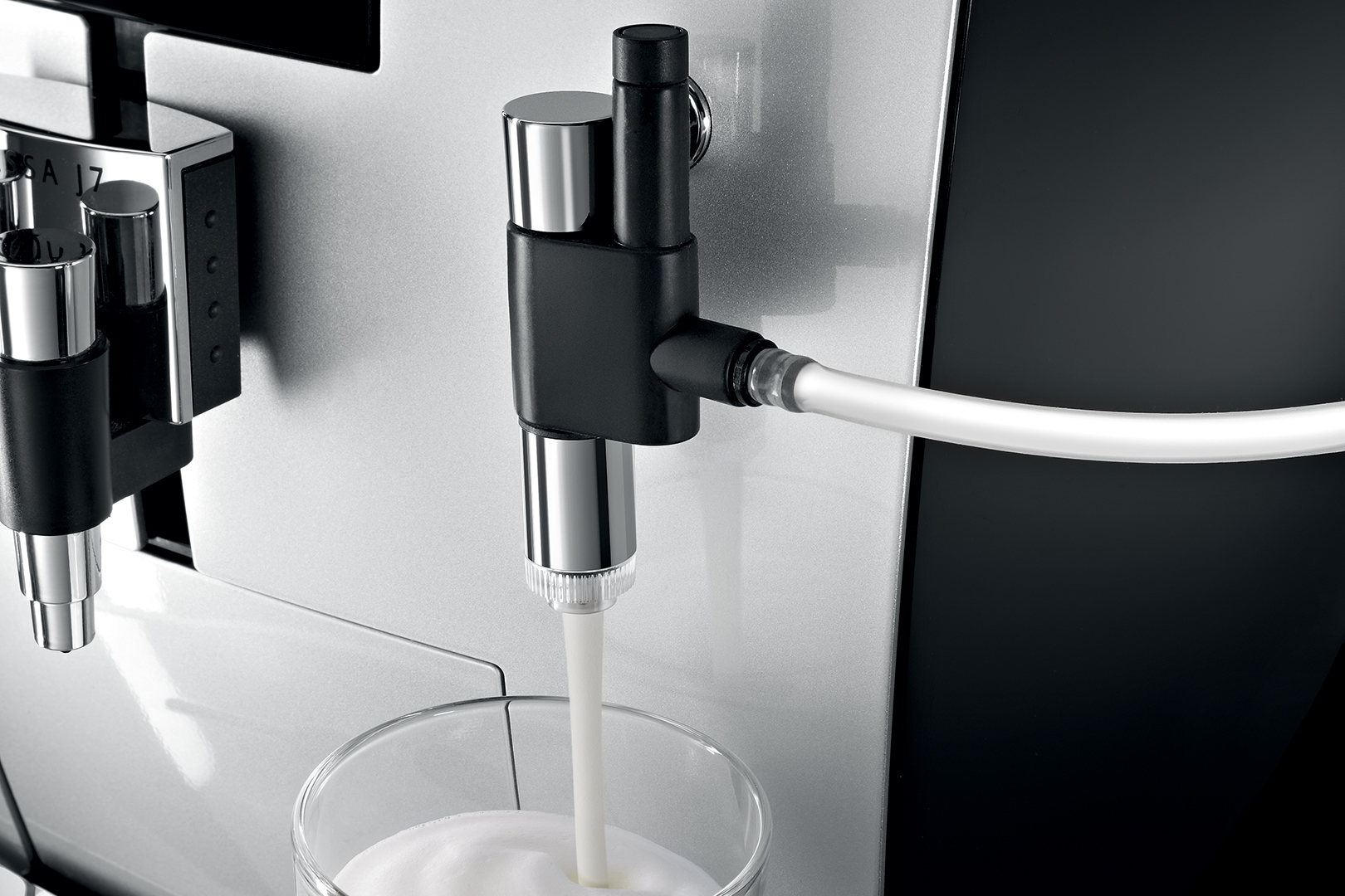 Nahaufnahme einer Kaffeemaschine, die Milch in ein Glas abgibt, mit einem weißen Schlauchanschluss.