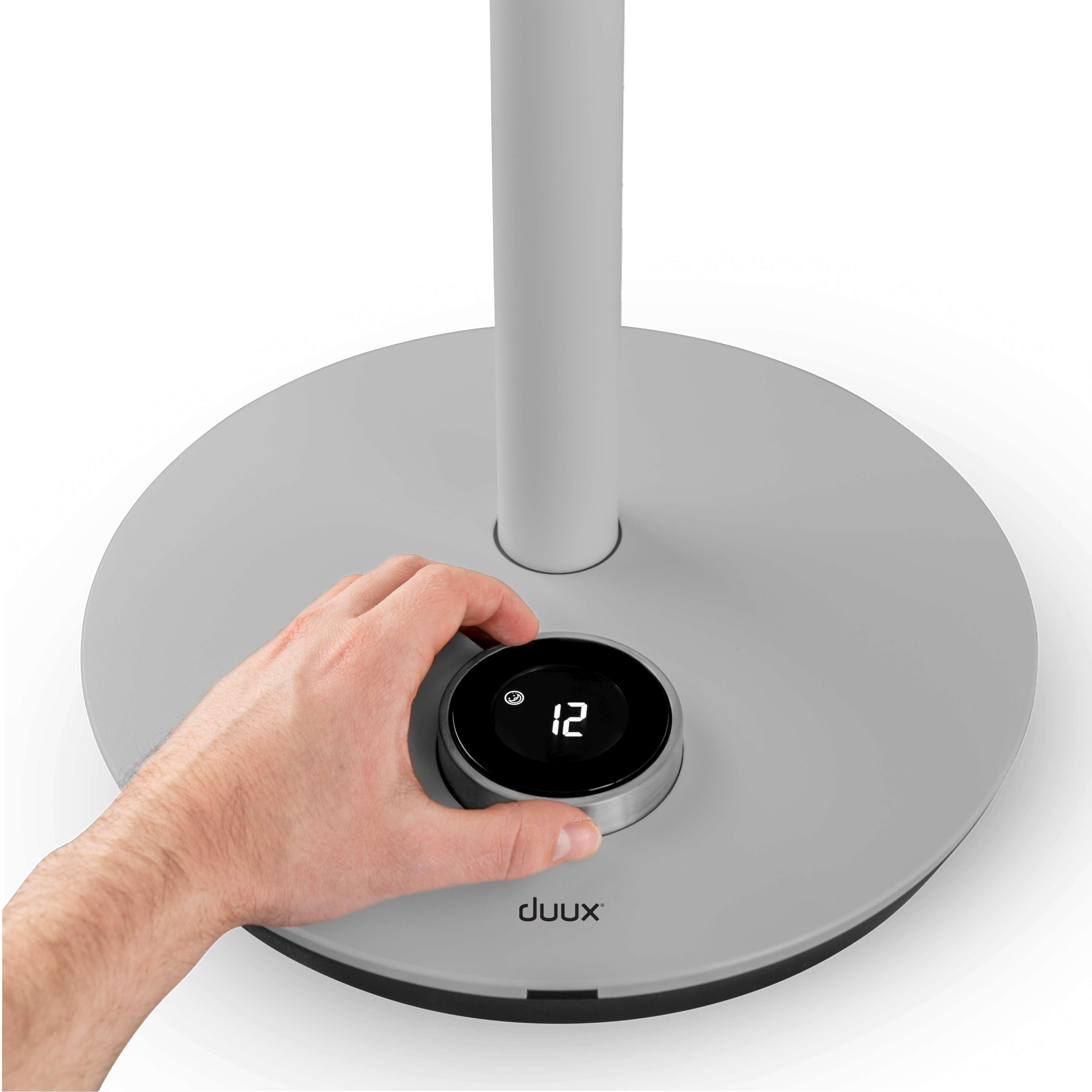 Hand stellt den Drehregler eines weiß-grauen Standventilators ein, zeigt die Zahl 12.