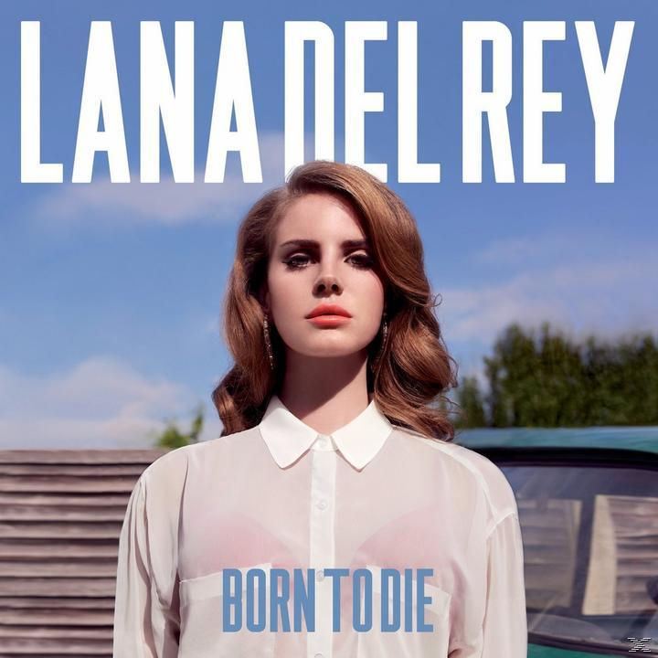 Lana Del Rey kint áll egy falemez fal és egy autó előtt.