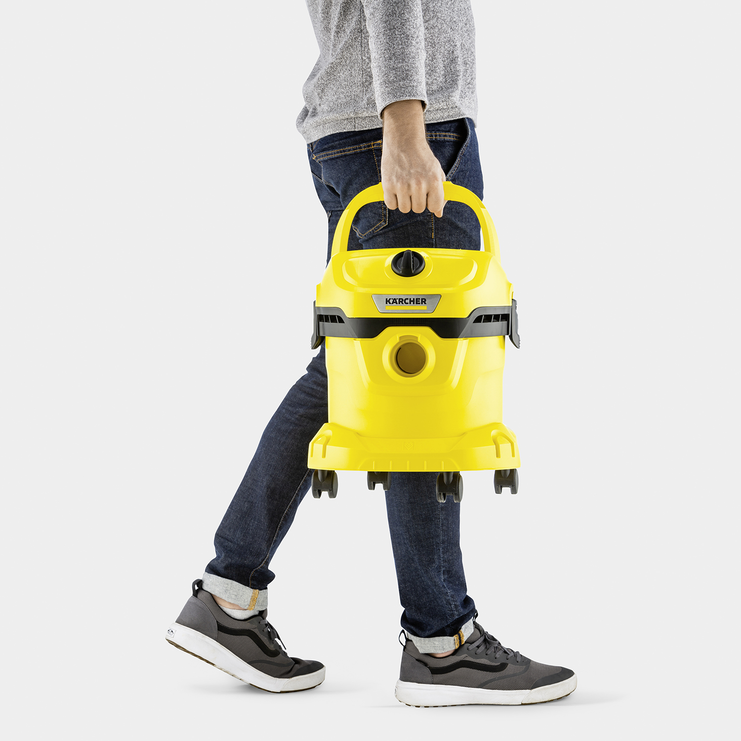 Persoon die loopt, met een gele Kärcher stofzuiger. Ze dragen een spijkerbroek, grijze top en sneakers.