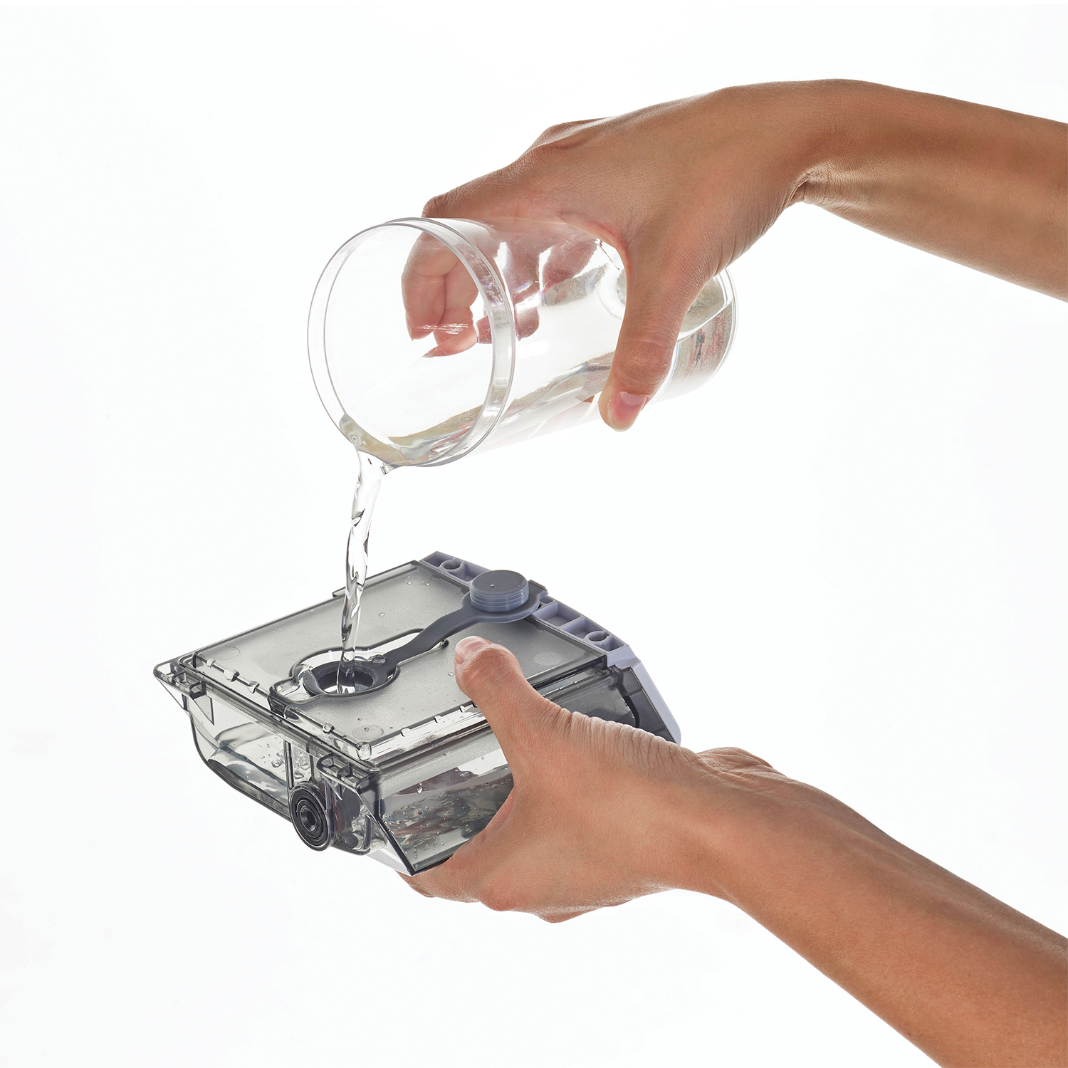 Mani che versano acqua da un bicchiere in un contenitore trasparente.