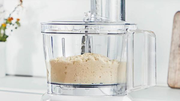 Küchenmaschine mit beigem Inhalt, teilweise gefüllt.